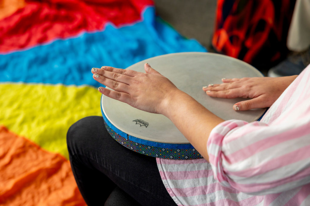 A person sitting with a drum in their lap and playing it with both hands.